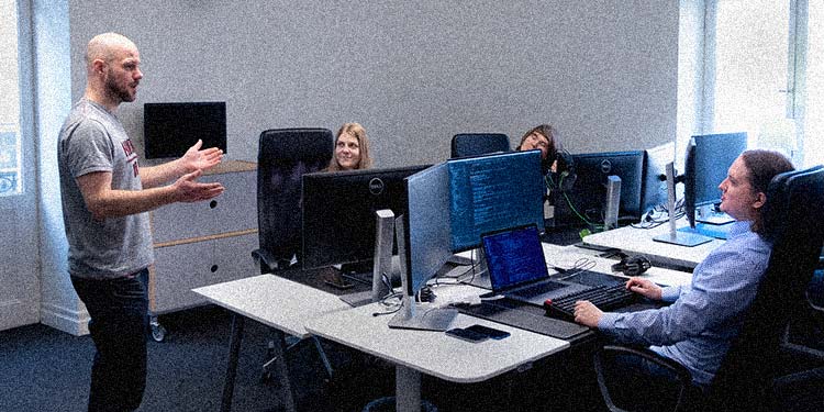 Medarbetare på Devize står och pratar till andra som sitter vid sina datorer